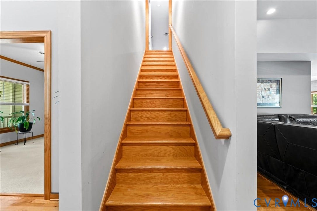 3060 Moyer Road, Powhatan, VA 23139 Straight staircase featuring warm wood-finish treads, white painted walls, and a natural wood handrail extending the full length of the passage for secure navigation between levels