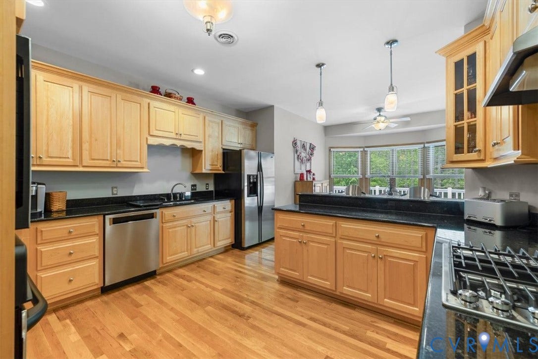 3060 Moyer Road, Powhatan, VA 23139 Spacious kitchen featuring natural wood cabinetry, black countertops, stainless steel appliances including a gas range and refrigerator, hardwood flooring, a large center island, pendant lighting, and abundant natural light from multi-pane windows