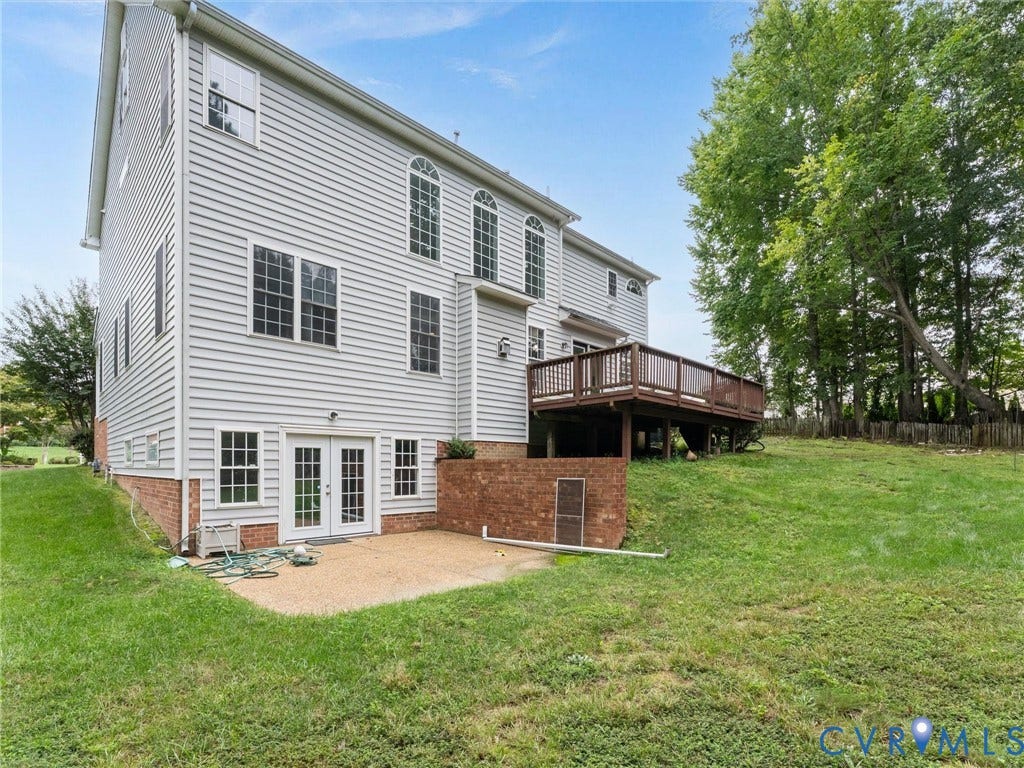 5017 Sadler Glen Place, Glen Allen, VA 23060 White siding exterior with multiple windows, a rear wood deck, a lower-level concrete patio, and a sloped grassy area