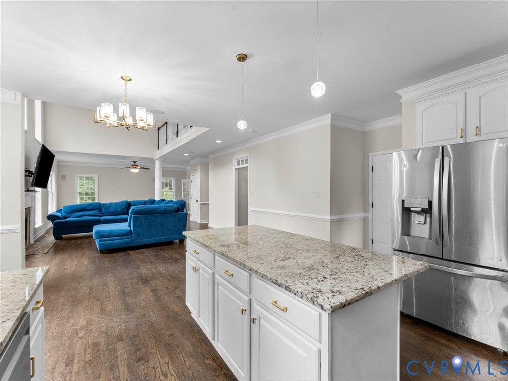 5017 Sadler Glen Place, Glen Allen, VA 23060 Open-concept living space featuring wood-finish flooring, a kitchen island with stone countertops, white cabinetry with gold-tone hardware, and a stainless steel refrigerator