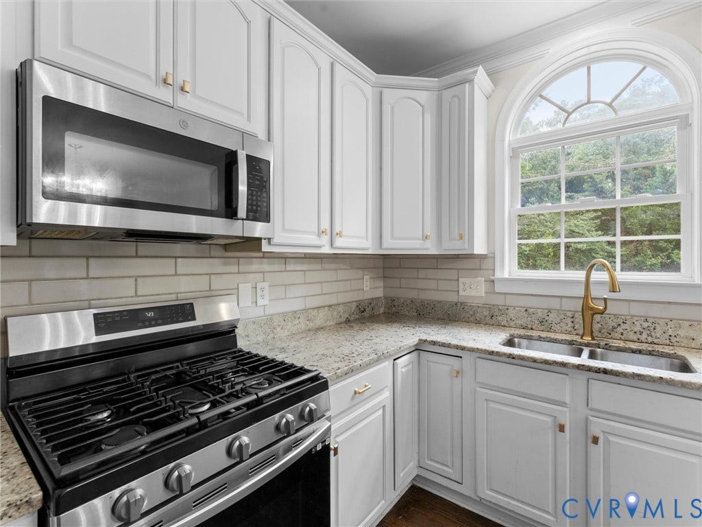 5017 Sadler Glen Place, Glen Allen, VA 23060 White cabinetry with gold-tone hardware, stainless steel appliances, granite-style countertops, subway tile backsplash, and an arched window