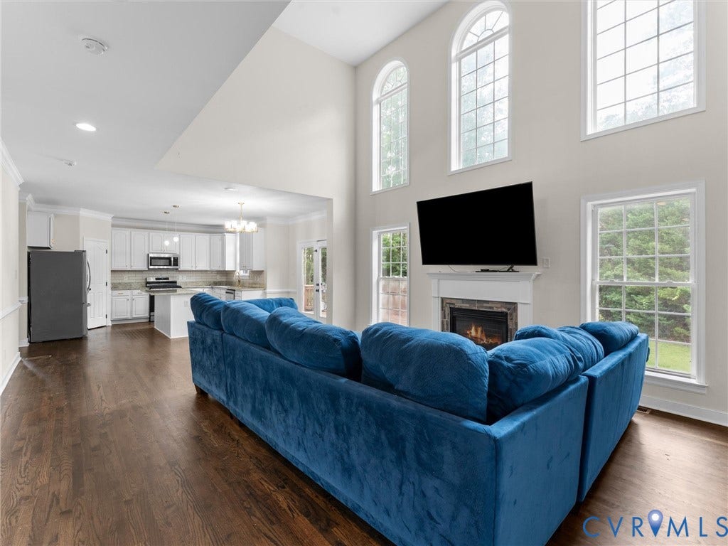 5017 Sadler Glen Place, Glen Allen, VA 23060 Vaulted ceilings with arched windows, wood-finish flooring, a fireplace with a stone surround, and an open-concept kitchen with white cabinetry