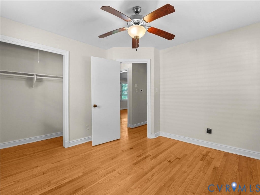 Hardwood flooring throughout, ceiling fan with integrated lighting, white trim, and a built-in closet with shelving and hanging rod