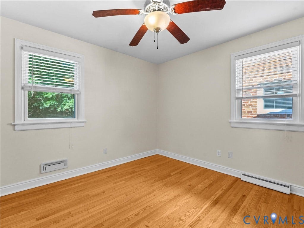 Wood-finish flooring, white trim, ceiling fan with integrated lighting, and two windows with blinds