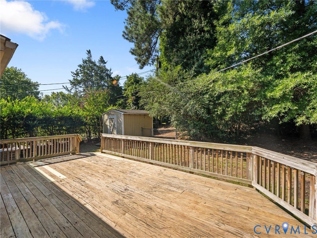 Expansive wood deck with a built-in railing system, featuring an outdoor storage shed and mature perimeter landscaping