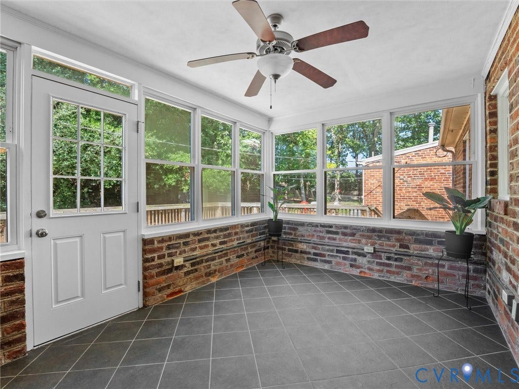 Enclosed sunroom featuring multiple windows, exposed brick walls, and a ceiling fan with integrated lighting