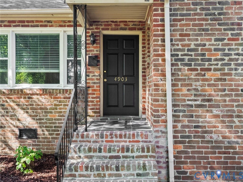 Brick exterior facade with a paneled front door, ornate wrought iron railing, and brick steps