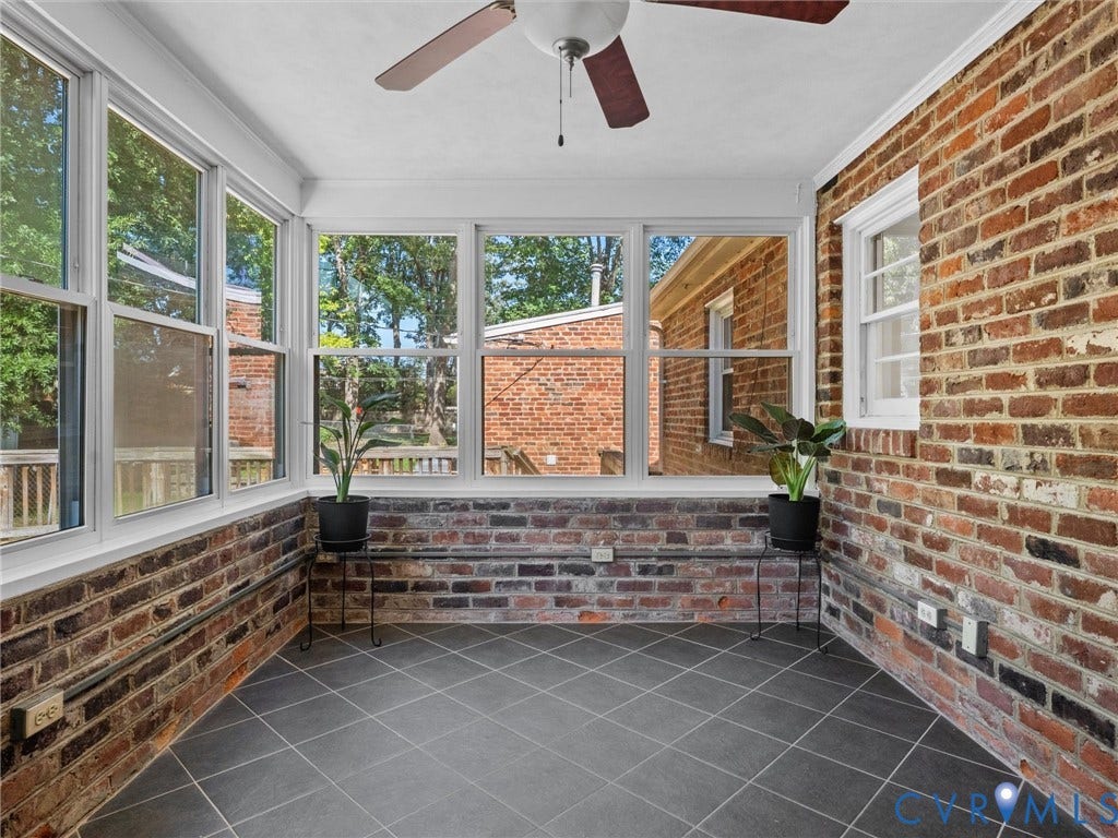 Sunroom featuring brick walls, a ceiling fan, multiple windows, and dark-toned tile flooring