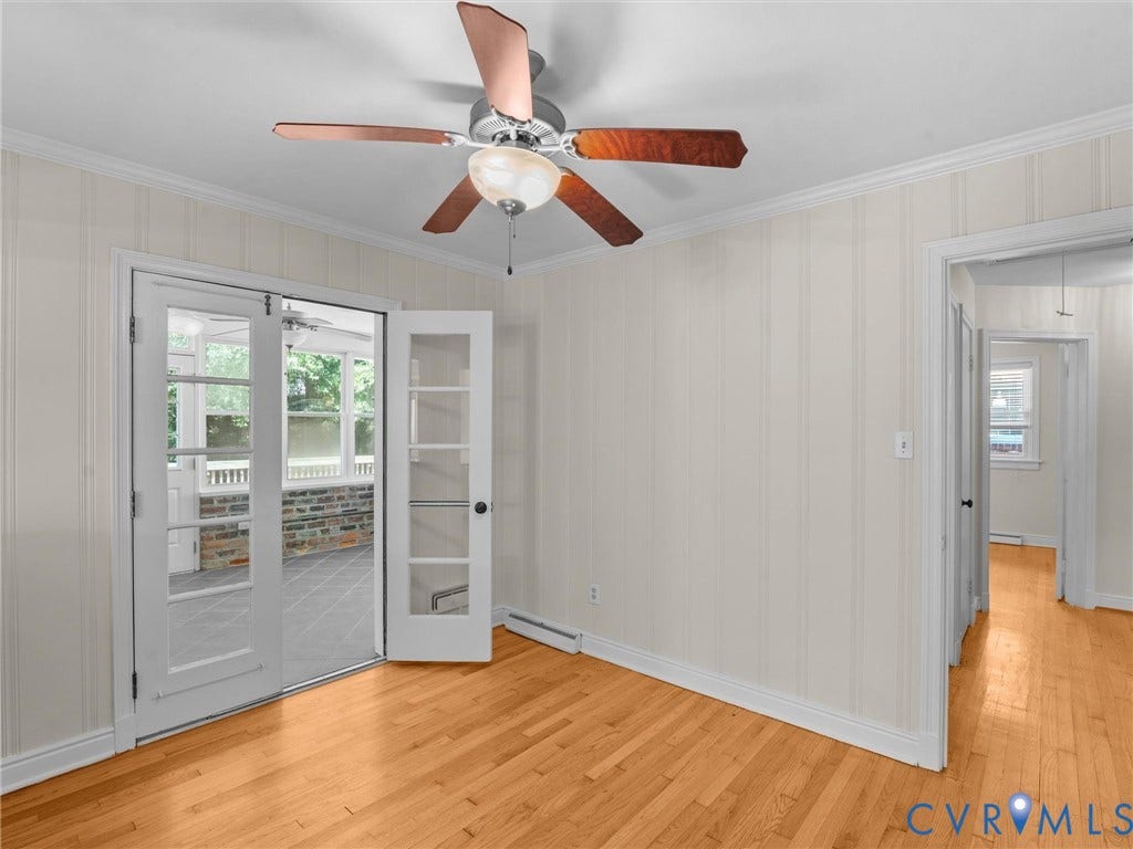 Wood-finish flooring, ceiling fan with integrated lighting, paneled walls, and French doors leading to an enclosed porch