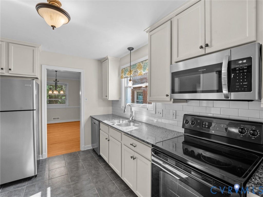 Stainless steel appliances, white subway tile backsplash, dark granite-style countertops, white cabinetry, and dark tile flooring