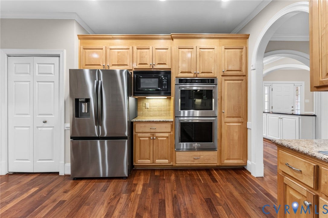 Wood-finish flooring, light wood cabinetry, stainless steel appliances, built-in double ovens, and a tiled backsplash