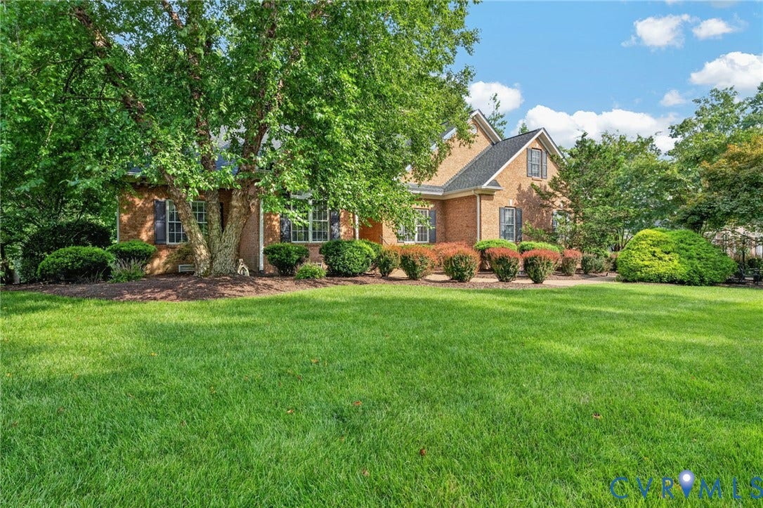 Brick Colonial residence showcasing a manicured front lawn, mature landscaping with established trees, and professionally maintained foundation plantings
