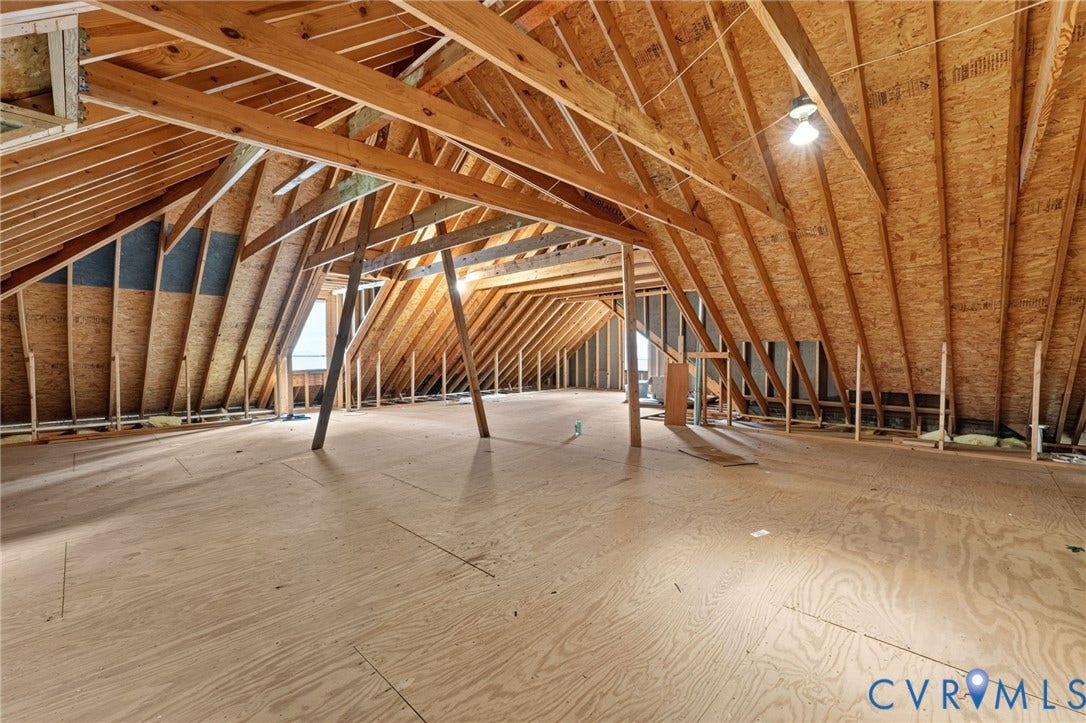 Expansive unfinished attic space featuring exposed wood framing, plywood flooring, and integrated lighting