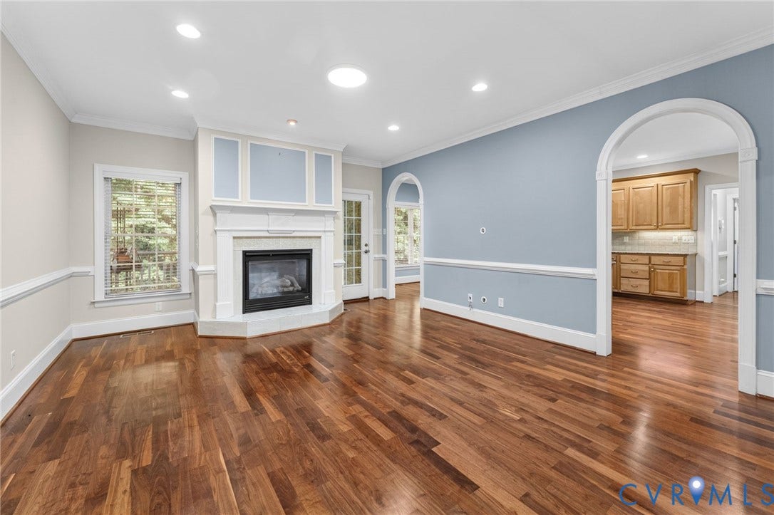 Elegant living space featuring hardwood flooring throughout, recessed ceiling lighting, and a gas fireplace with white surround and built-in shelving