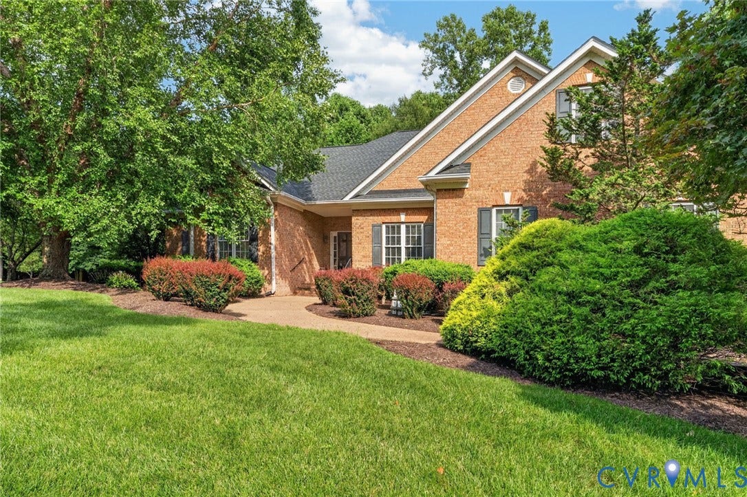 Brick exterior with gabled roofline, featuring a concrete pathway, manicured lawn, and mature trees