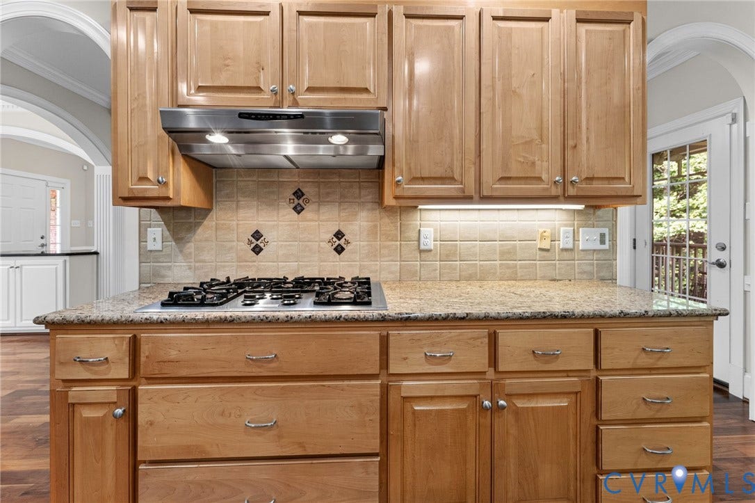 Kitchen featuring wood cabinetry, a gas cooktop, granite-style countertops, a tile backsplash with decorative accents, and stainless steel range hood