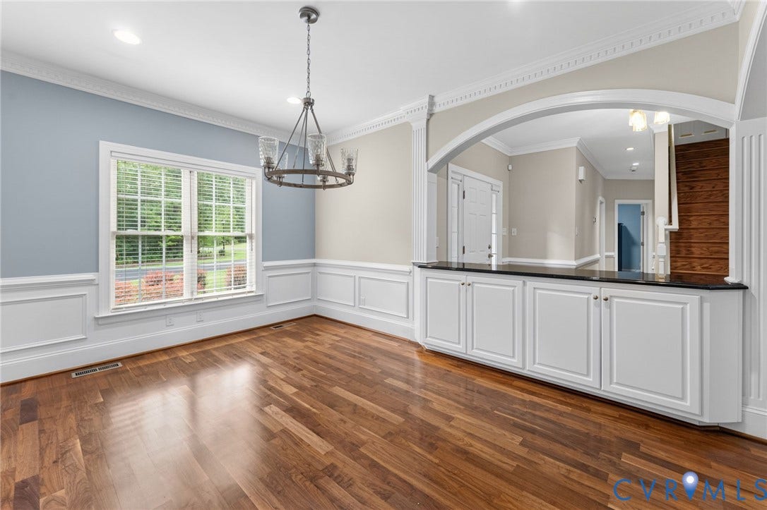 Wood-finish flooring, wainscoting, crown molding, built-in cabinetry with a dark countertop, and an arched entry