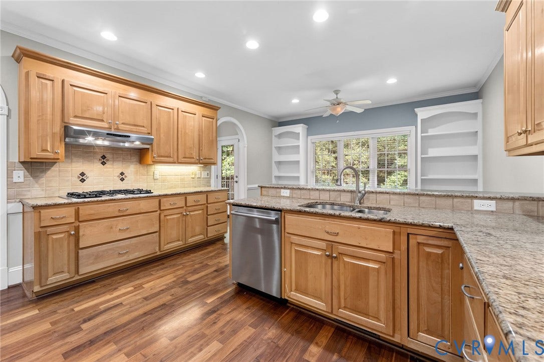 Chef's kitchen featuring custom wood cabinetry, stainless steel appliances, granite countertops, tile backsplash, and a large center island with seating
