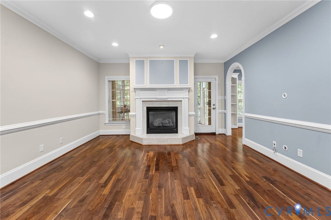 Elegant living space showcasing rich wood-finish flooring, recessed ceiling lighting, and a custom white fireplace surround with gas insert