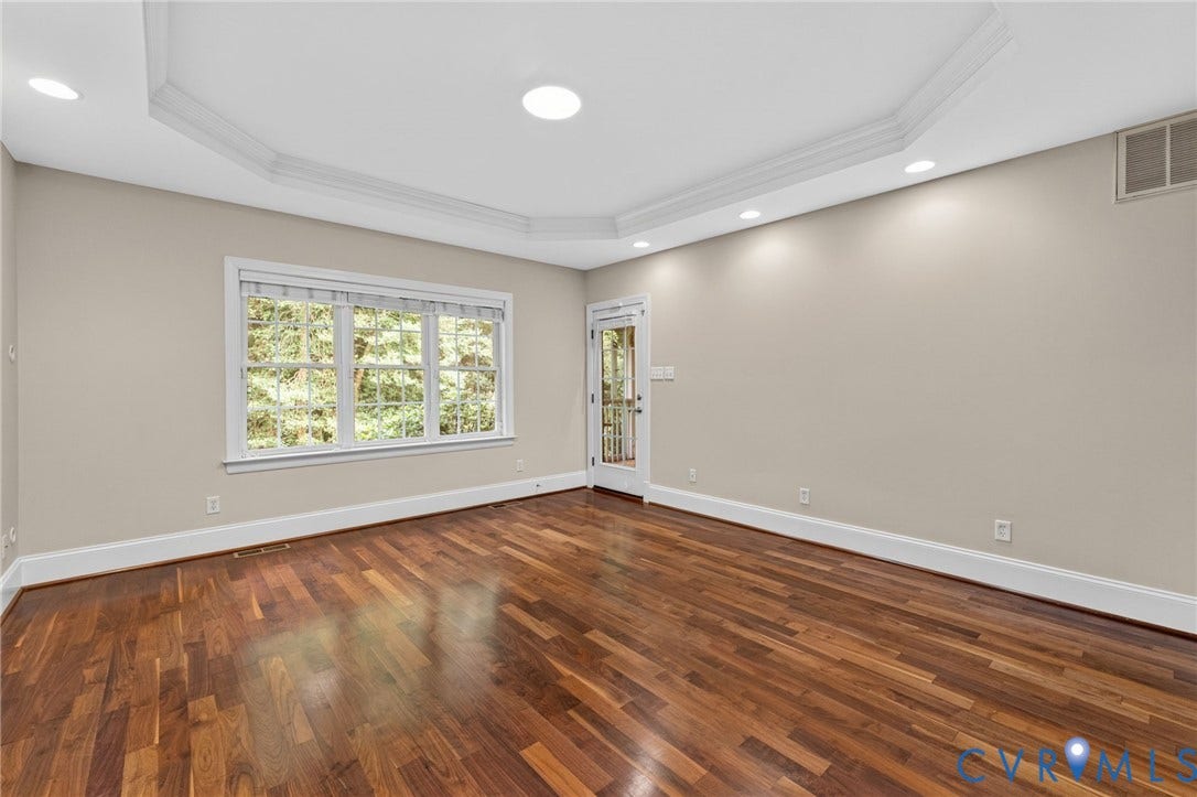Spacious room featuring rich wood-finish flooring, recessed ceiling lighting, and abundant natural light from a triple-window configuration
