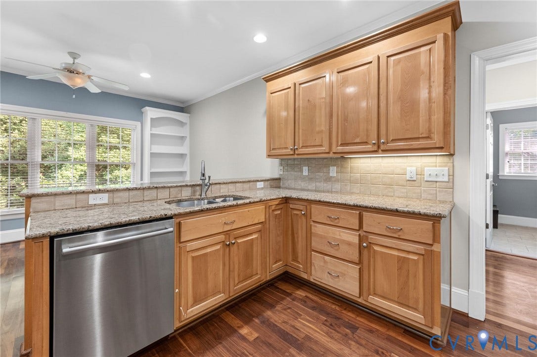Warm wood cabinetry with raised-panel doors and brushed hardware anchors this kitchen, featuring stainless steel appliances, subway tile backsplash, and dark countertops