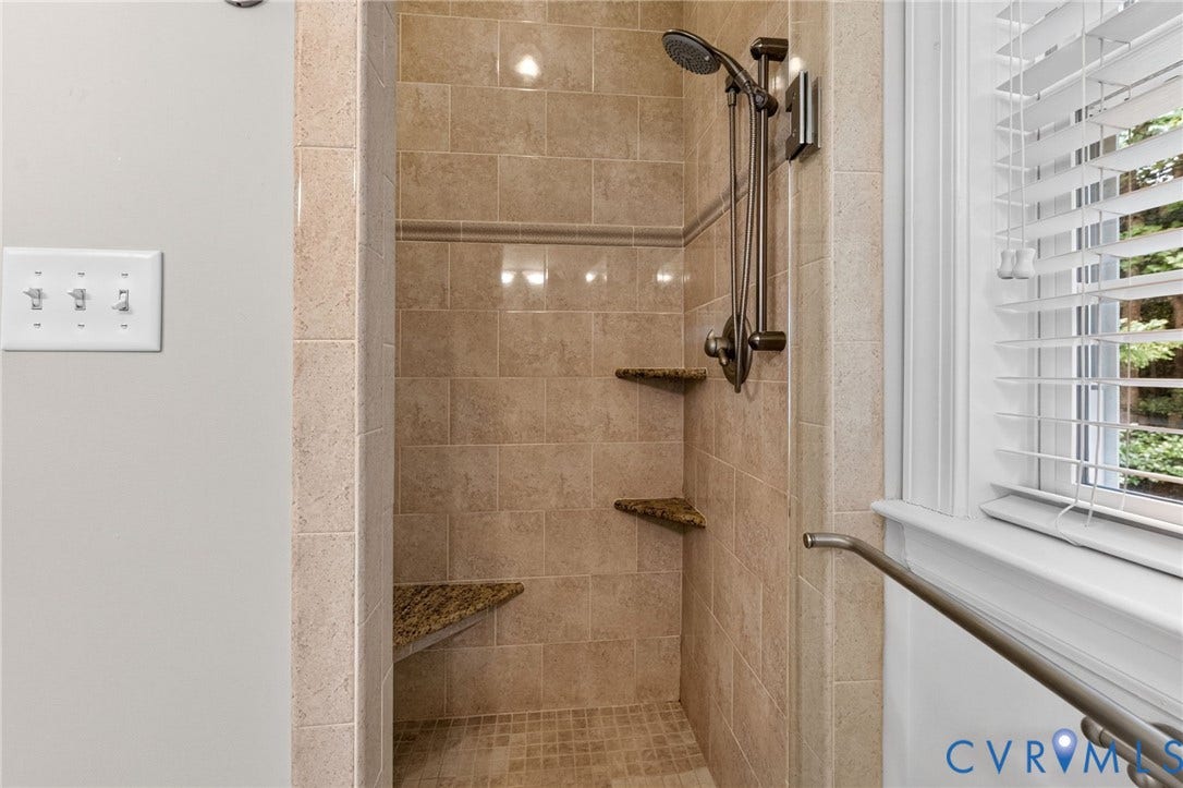 Tiled shower with handheld shower fixture, built-in corner shelves, and a built-in bench