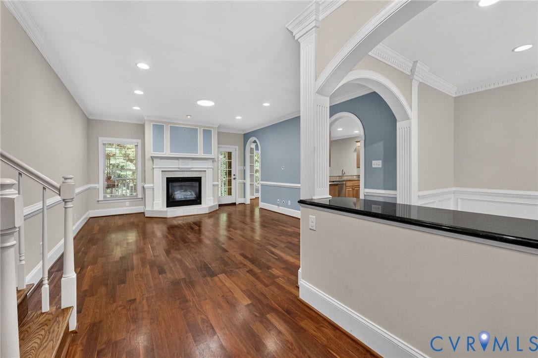 Hardwood flooring, recessed lighting, corner fireplace with white mantel, interior archways, and a dark countertop