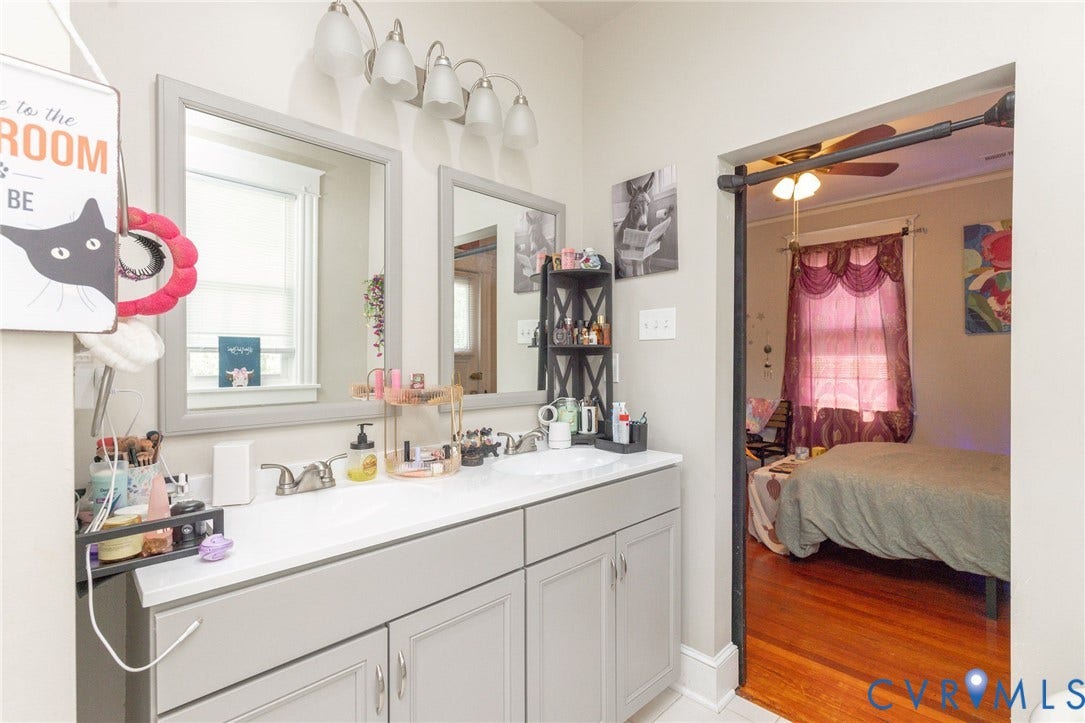 2726 Hanes Avenue, Brookland Park, Richmond, VA 23222 Dual framed mirrors with sconce lighting, double vanity with base cabinetry, and a connecting doorway to a room with wood flooring