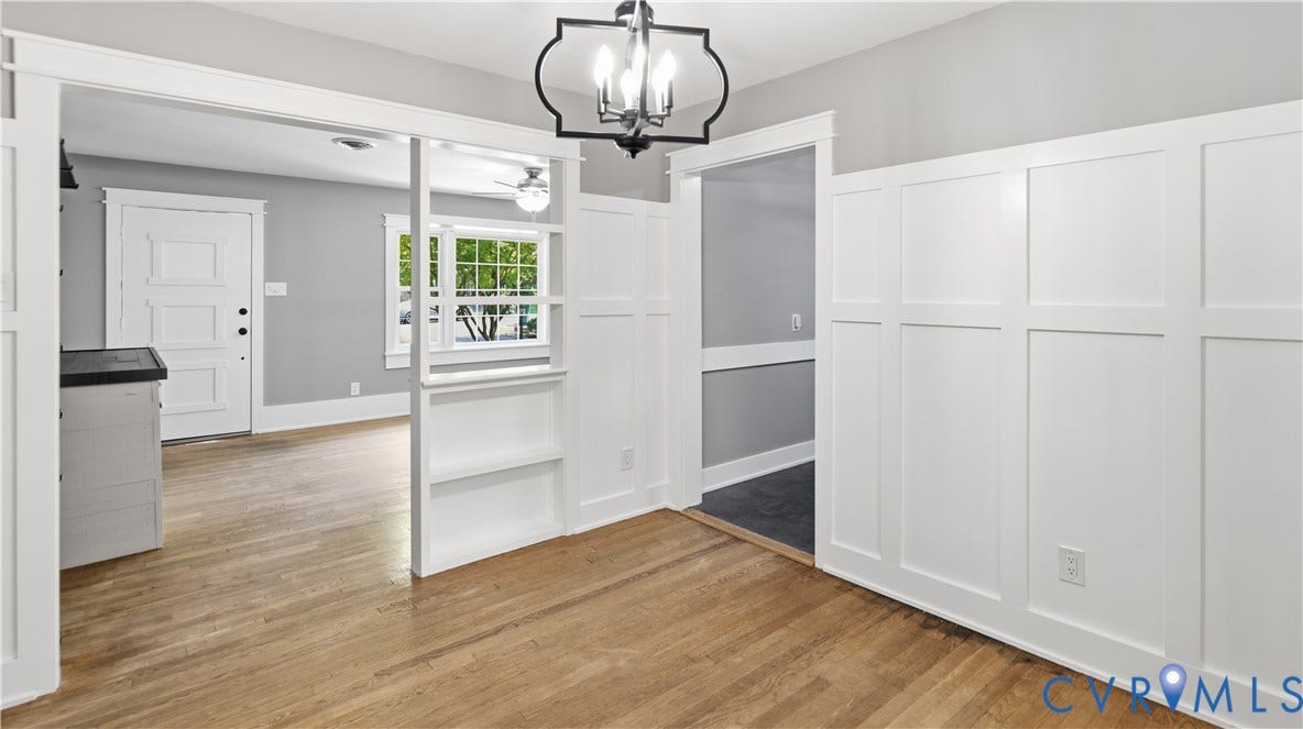 Hardwood flooring, painted board and batten wall, built-in shelving, black metal chandelier, and a paneled front door