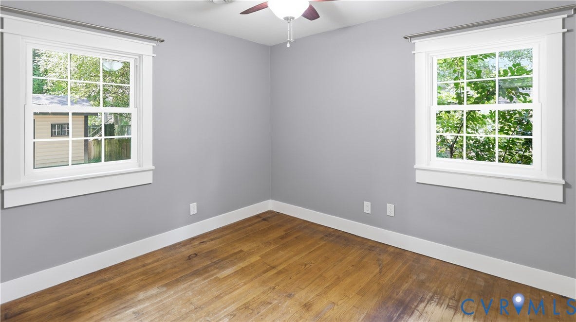 Hardwood flooring, two large windows, white window trim, contemporary gray wall paint, and a ceiling fan with integrated lighting