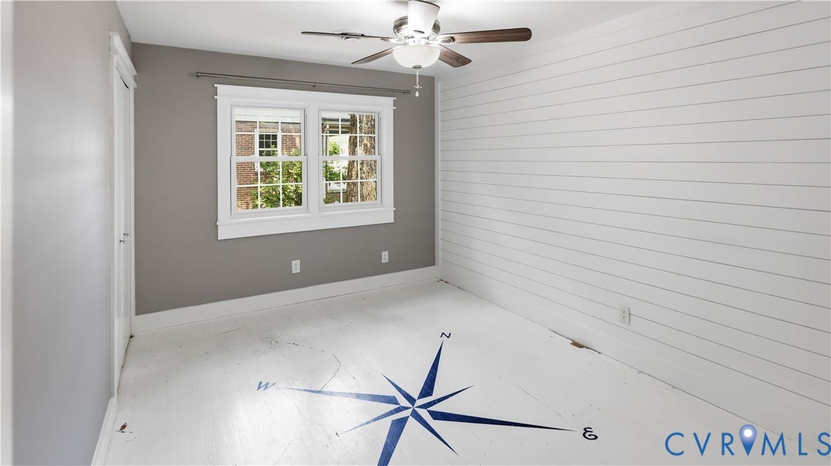 White shiplap accent wall, white wood-finish flooring with a compass design, ceiling fan with light fixture, and a double window with white trim