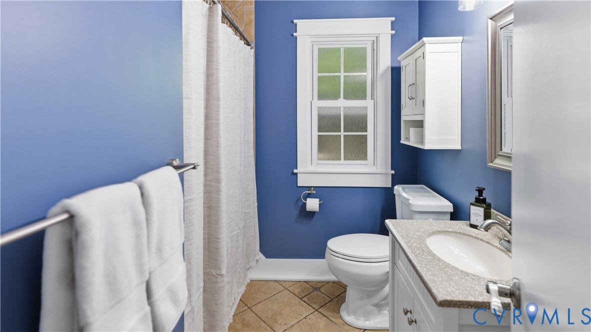 Bathroom featuring a single window, white vanity with integrated sink, white storage cabinet, toilet, and tiled flooring