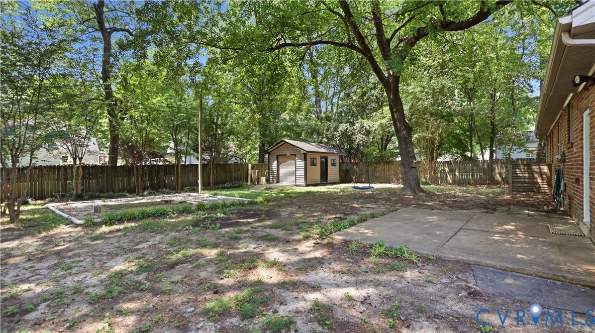 Expansive backyard featuring a privacy fence, mature trees, concrete patio, and a storage shed