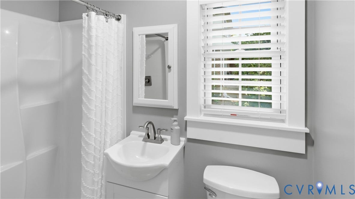 White shower/tub combination, single vanity with integrated sink, white medicine cabinet, and window with white blinds