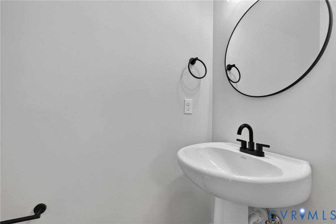 6541 Hardee Haven Place, Midlothian, VA 23112 Pedestal sink with a matte black two-handle faucet, round wall mirror, and matte black towel rings