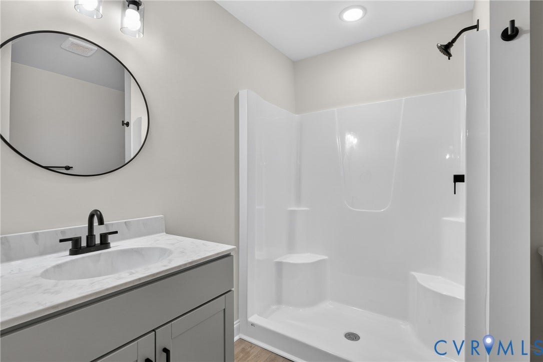 6541 Hardee Haven Place, Midlothian, VA 23112 Vanity with an integrated sink and stone-finish countertop, matte black faucet, framed round mirror, overhead vanity lighting, and a walk-in shower with built-in seating
