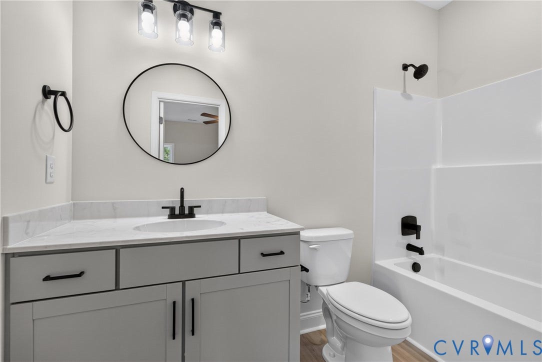 6541 Hardee Haven Place, Midlothian, VA 23112 Bathroom featuring a white integrated sink, light gray vanity with black hardware, black-framed round mirror, and a tub/shower combination with black fixtures
