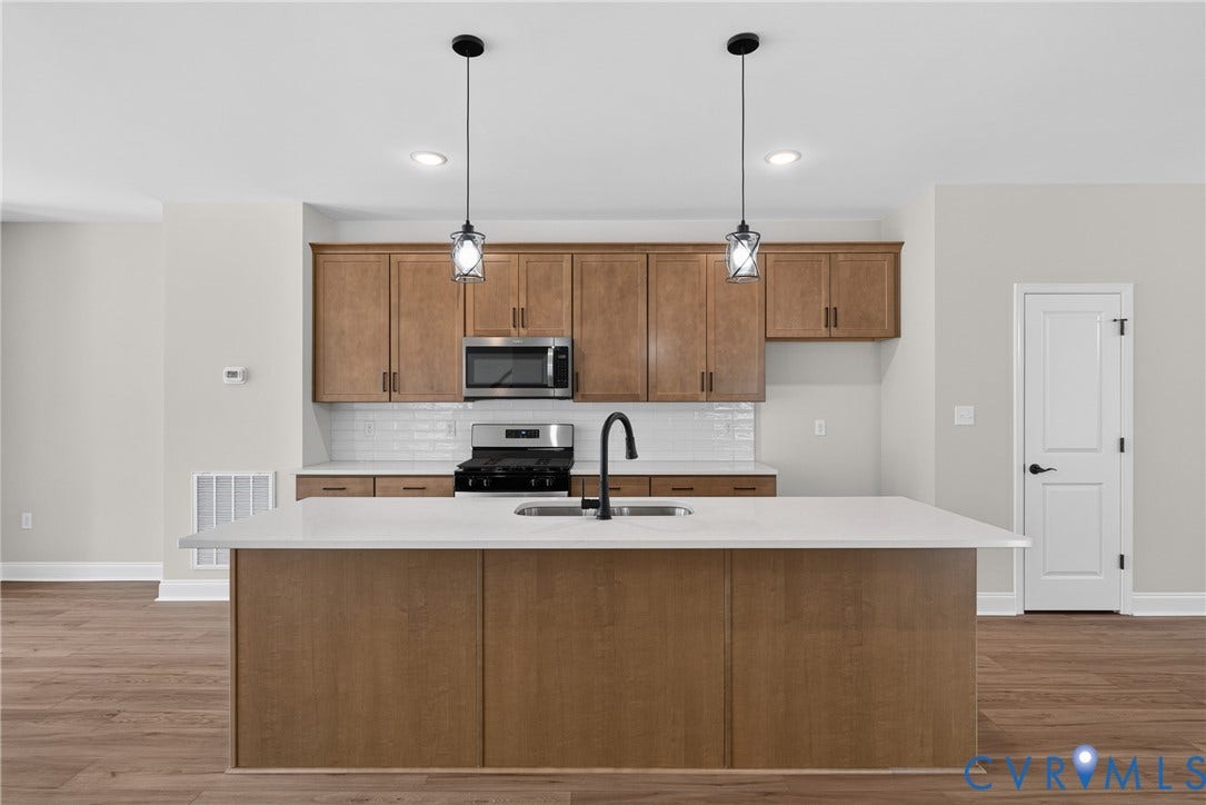 6549 Hardee Haven Place, Midlothian, VA 23112 Kitchen featuring wood-finish cabinetry, stainless steel appliances, a white subway tile backsplash, and an island with a white countertop and double sink