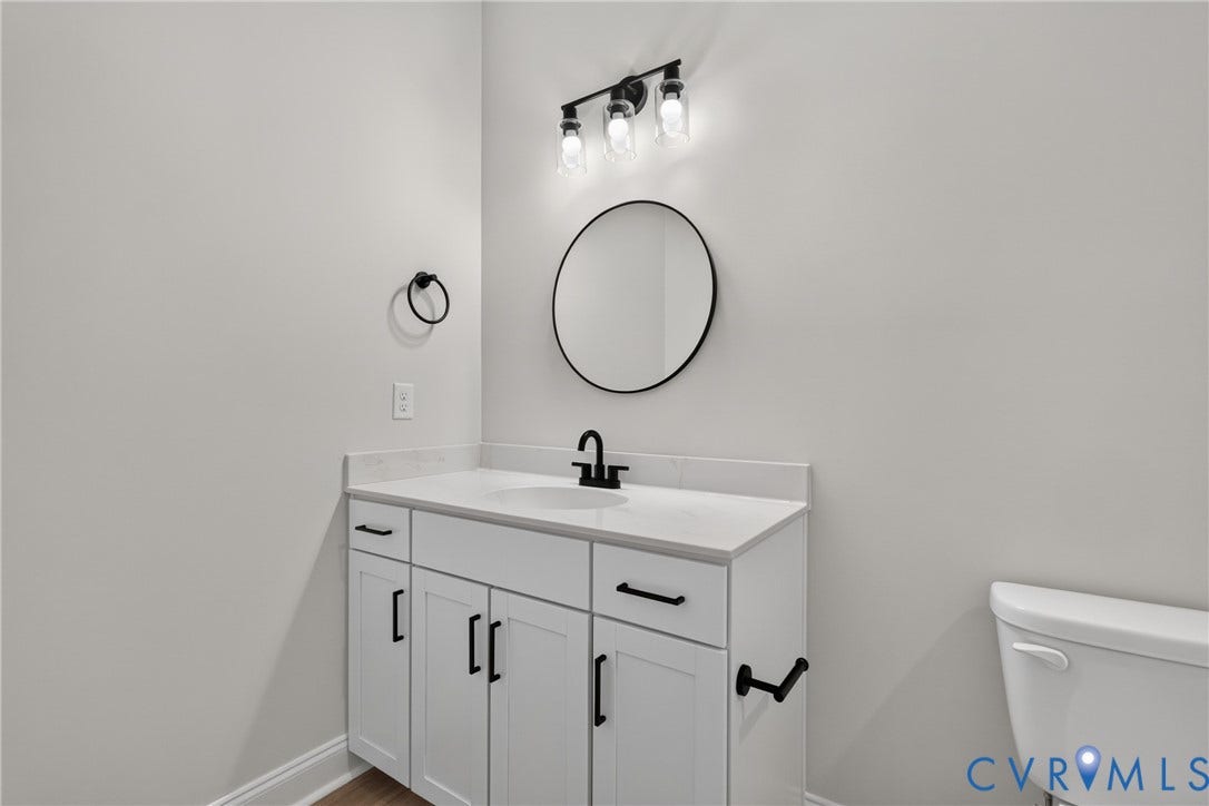 6549 Hardee Haven Place, Midlothian, VA 23112 White vanity with black hardware, white countertop, round mirror, and wall-mounted light fixture