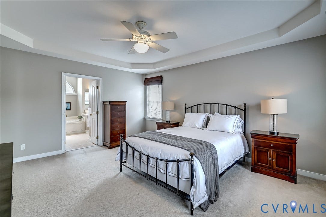 Recessed ceiling with a ceiling fan, carpet flooring, and a private ensuite bathroom.