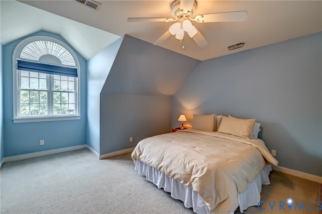 Window with arched transom and custom window treatment, sloped ceiling, ceiling fan with integrated lighting, and carpeted flooring