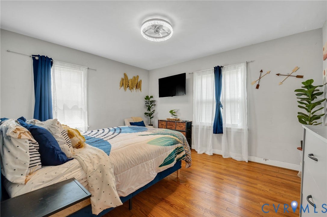 4819 Arundel Avenue, Chesterfield, VA 23234 Bright, spacious bedroom featuring hardwood flooring, dual glass doors with sheer and blue drapery, wall-mounted flat-screen television, ceiling fan with integrated lighting, and ample natural light from multiple windows
