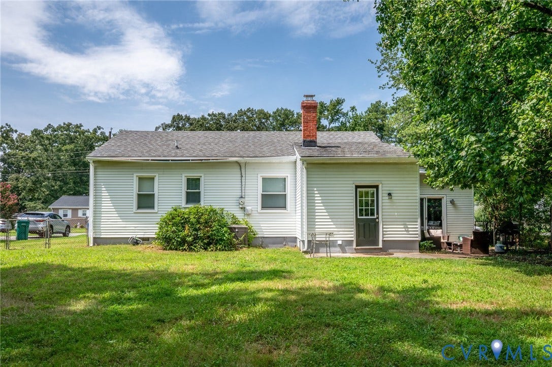4819 Arundel Avenue, Chesterfield, VA 23234 Rear exterior featuring white horizontal siding, a red brick chimney, a dark paneled door with glass inserts, and a concrete patio