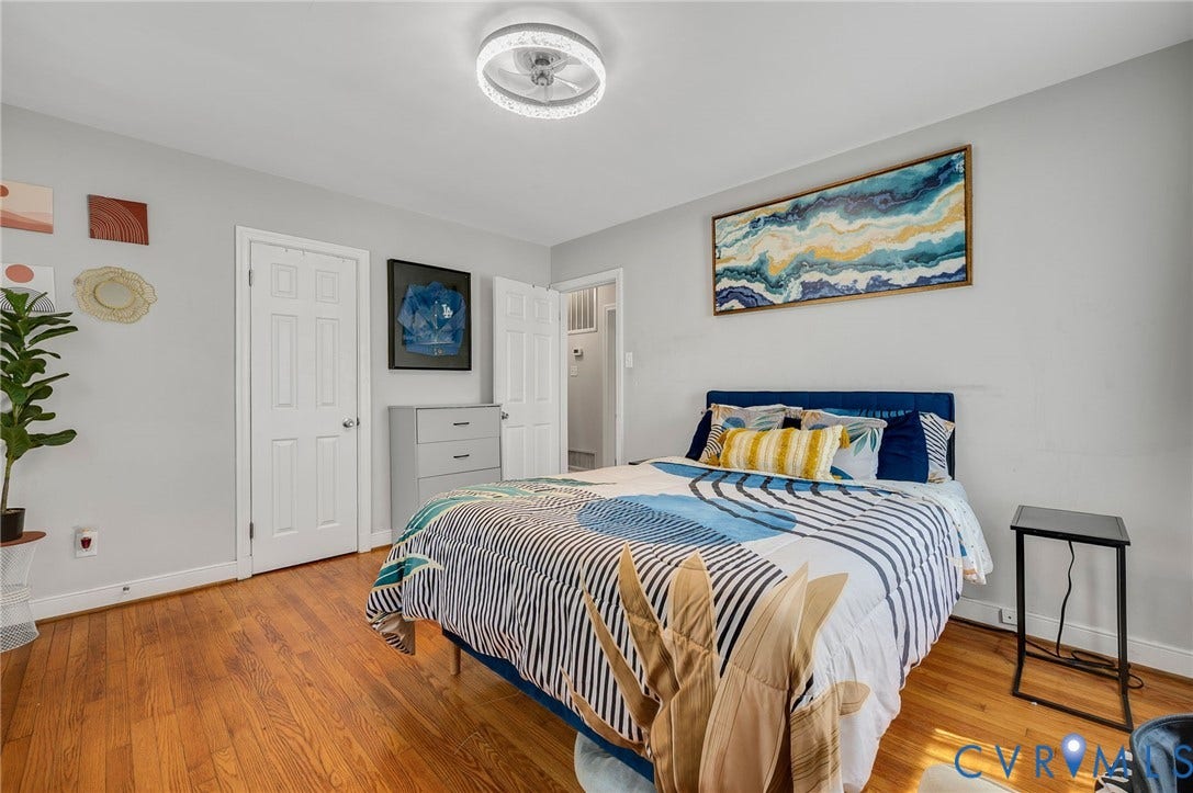 4819 Arundel Avenue, Chesterfield, VA 23234 Bright secondary bedroom featuring hardwood flooring, a queen-sized bed frame with blue and gold upholstered headboard, large windows providing natural light, and multiple closet access points