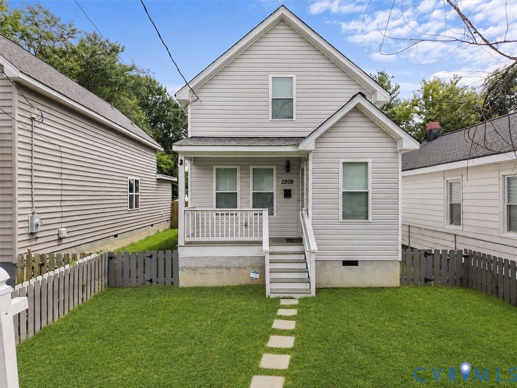Siding exterior, covered porch, white railings, front yard with stone path, and a fenced perimeter