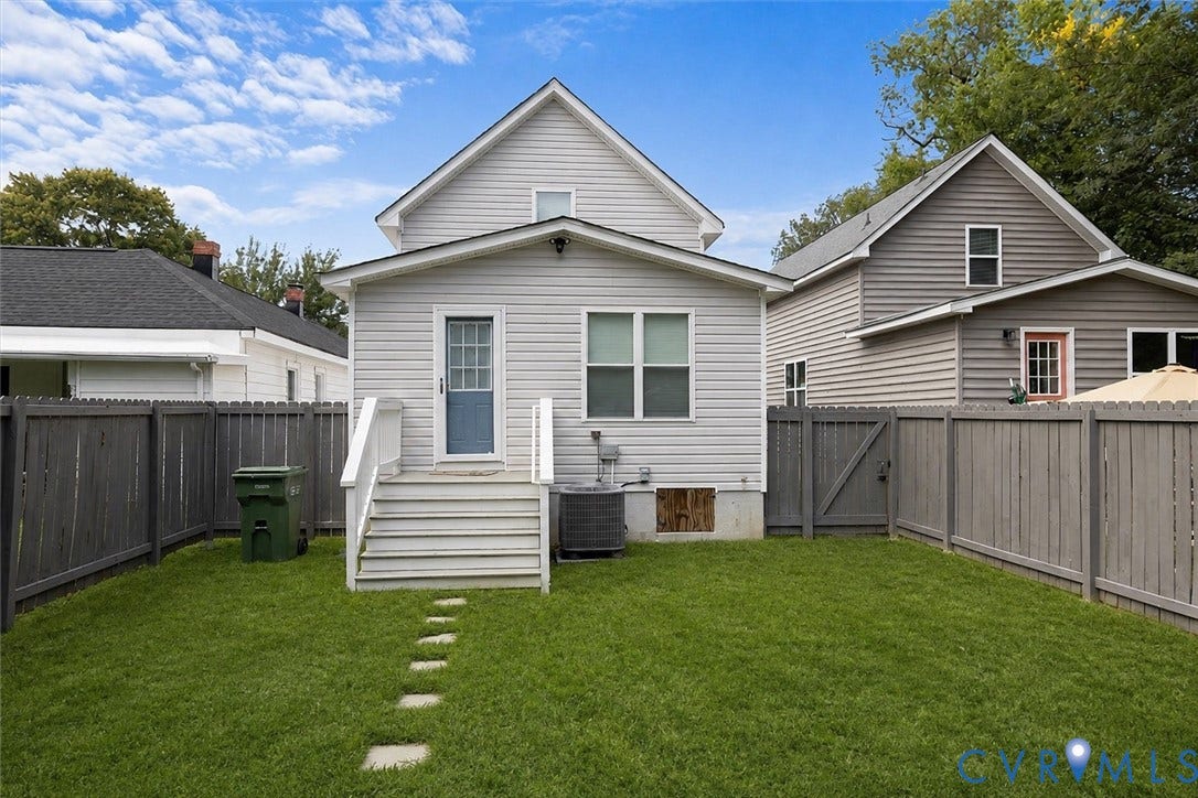 Manicured lawn with stepping stones, featuring a wood fence, exterior steps with railings, and a side entry door