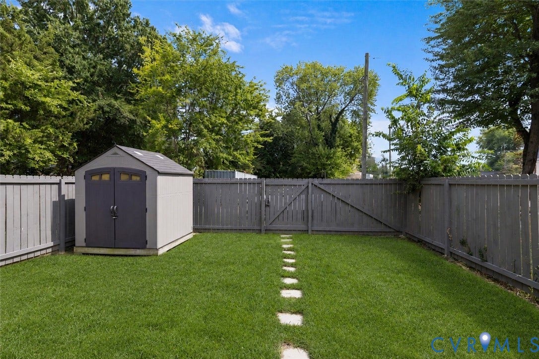 Fenced yard featuring a storage shed, a lawn area, and a stepping stone pathway