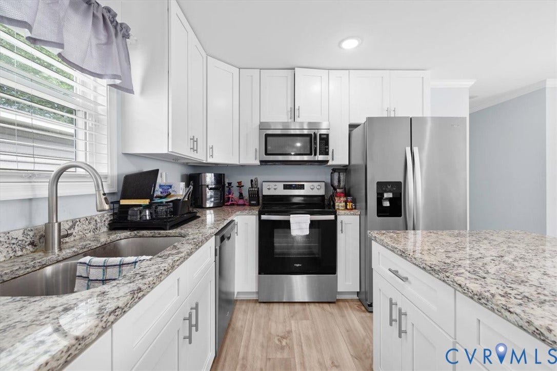 Bright kitchen featuring white shaker cabinetry, stainless steel appliances, granite countertops, wood-finish flooring, and a large kitchen island