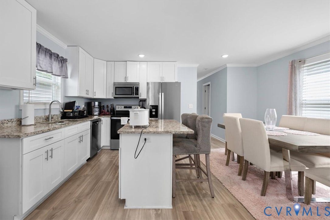 Open-concept kitchen and dining area featuring white cabinetry, stainless steel appliances, a center island with bar seating, and wood-finish flooring