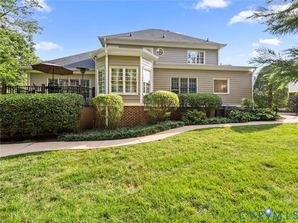 15706 Fox Marsh Drive, Moseley, VA 23120 Expansive lawn featuring a concrete pathway, a raised deck with dark railings, a bay window, and established landscaping